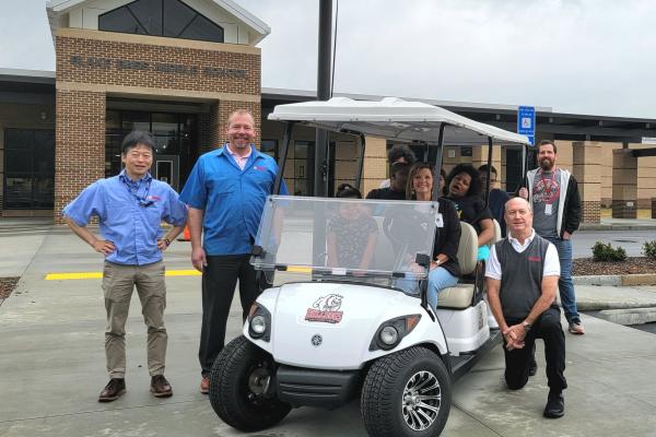 Yamaha delivers a custom golf car to Blake Bass Middle. Pictured are Yamaha President Taka Imanishi, Yamaha VP Bob Brown, Principal Cindy Bennett, Yamaha VP Wayne Pierce, and Teacher Connor Cody along with Blake Bass students.